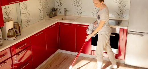 Young woman vacuums the floor with a cordless vacuum cleaner in a red kitchen.